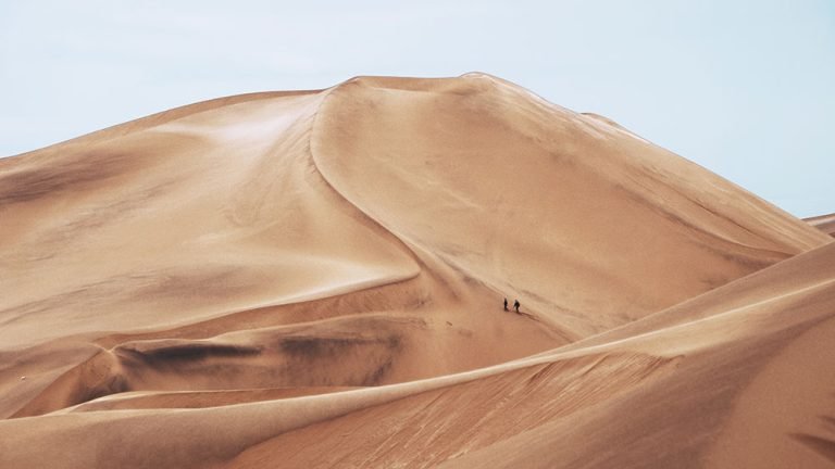 Hikers climbing massive sand dunes in a desert landscape.